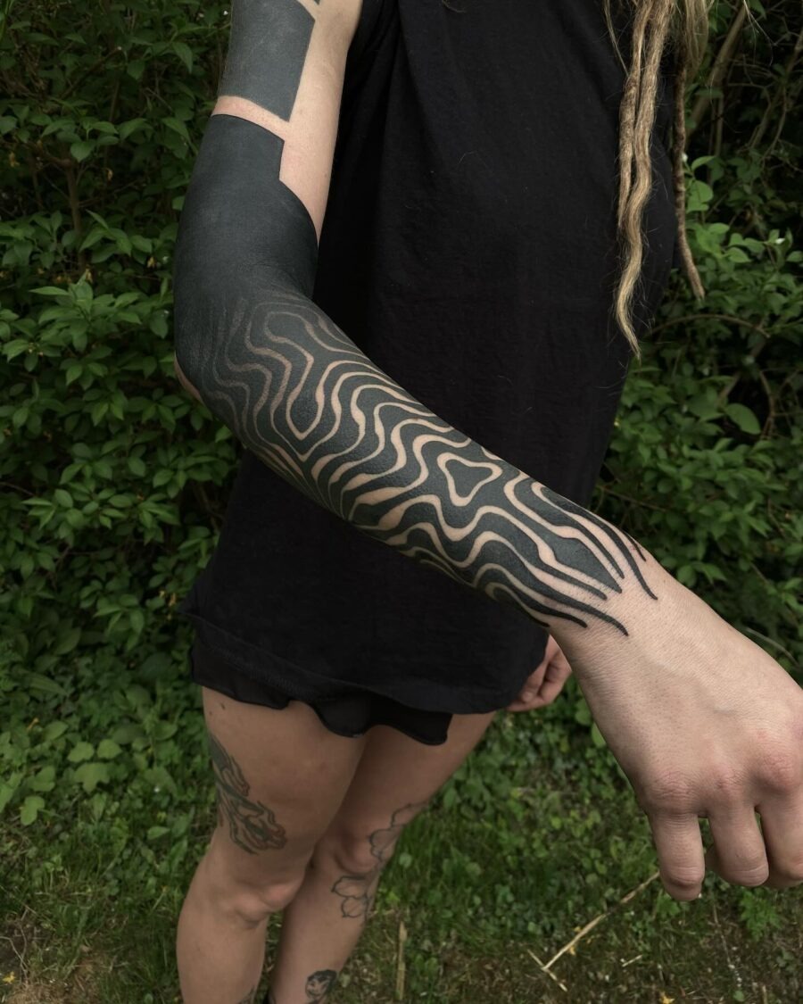 This tattoo features intricate black designs that flow elegantly along the arm.