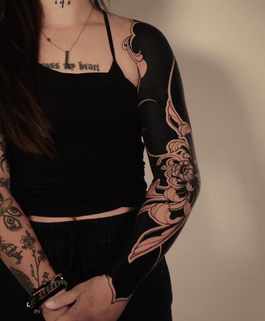 This black sleeve tattoo features intricate floral patterns that flow elegantly across the arm.