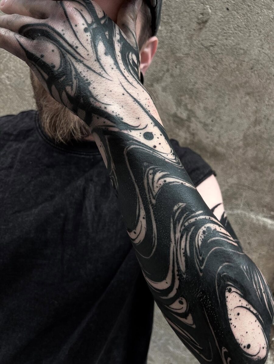 This black sleeve tattoo blends striking black ink with subtle skin tone patterns, creating a mesmerizing marbled effect.