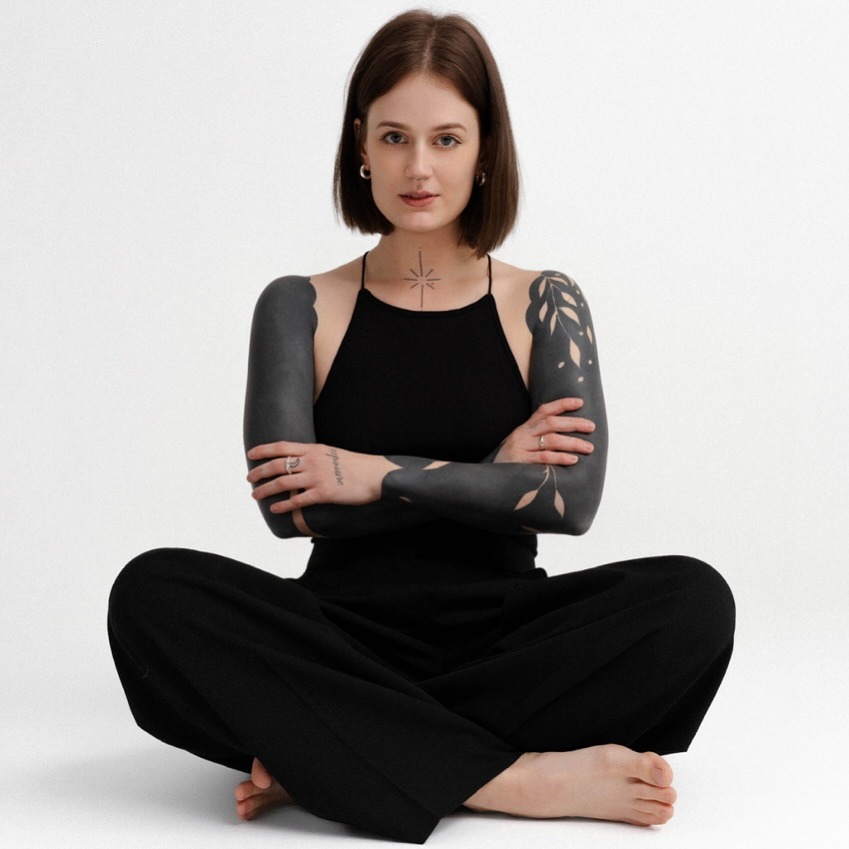 This image features a model showing intricate black sleeve tattoos that blend bold patterns with subtle details.