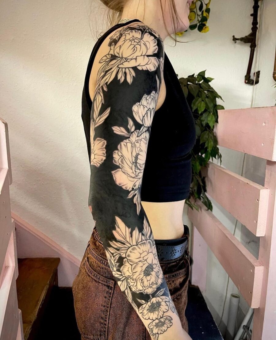 This striking sleeve tattoo features intricate floral patterns against a bold black background.