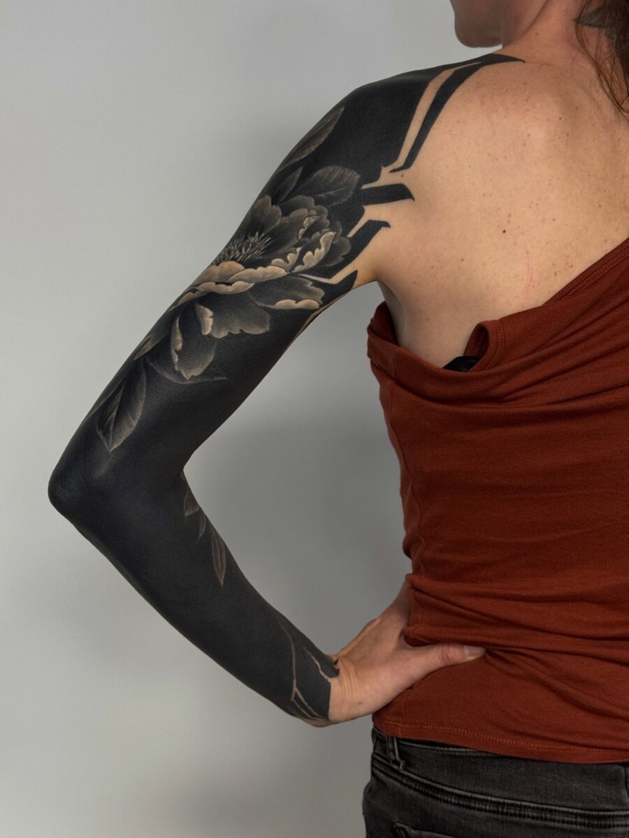 This stunning black sleeve tattoo features intricate floral designs intertwined with bold, dark shading.