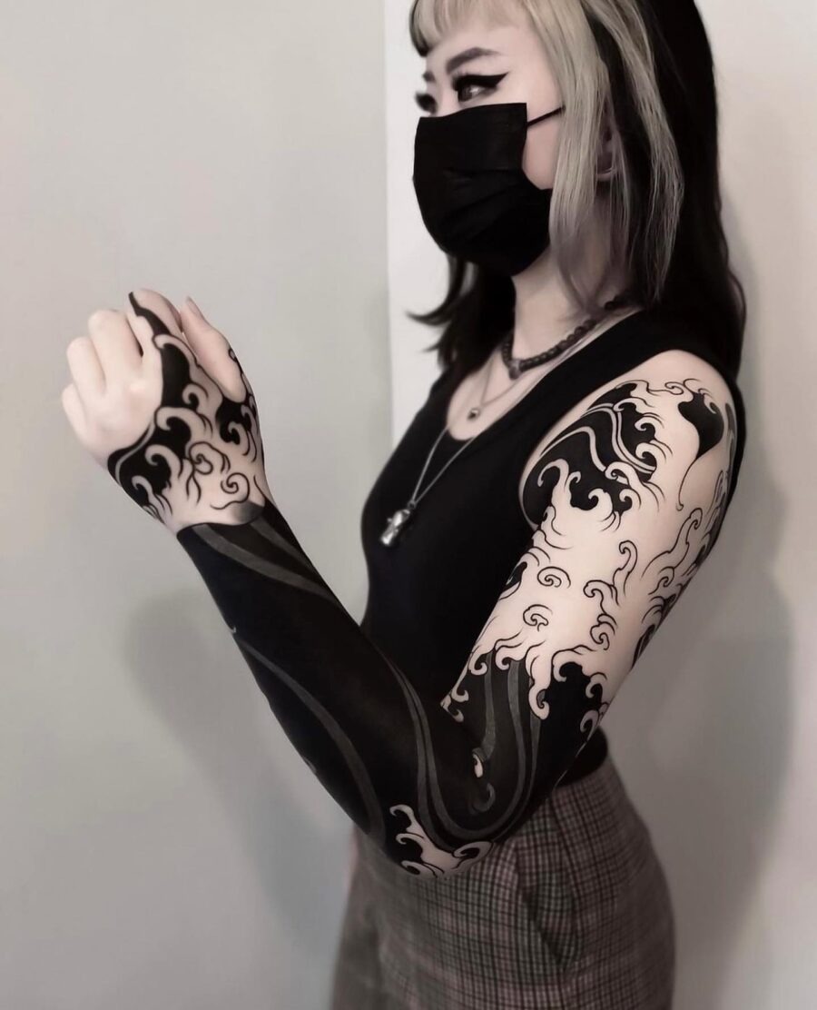 This striking black sleeve tattoo showcases intricate wave designs that flow beautifully around the arm.