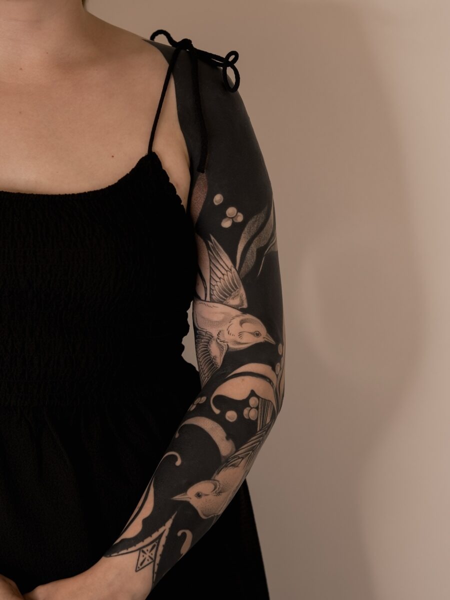 This stunning black sleeve tattoo showcases intricate birds and swirling foliage throughout its design.