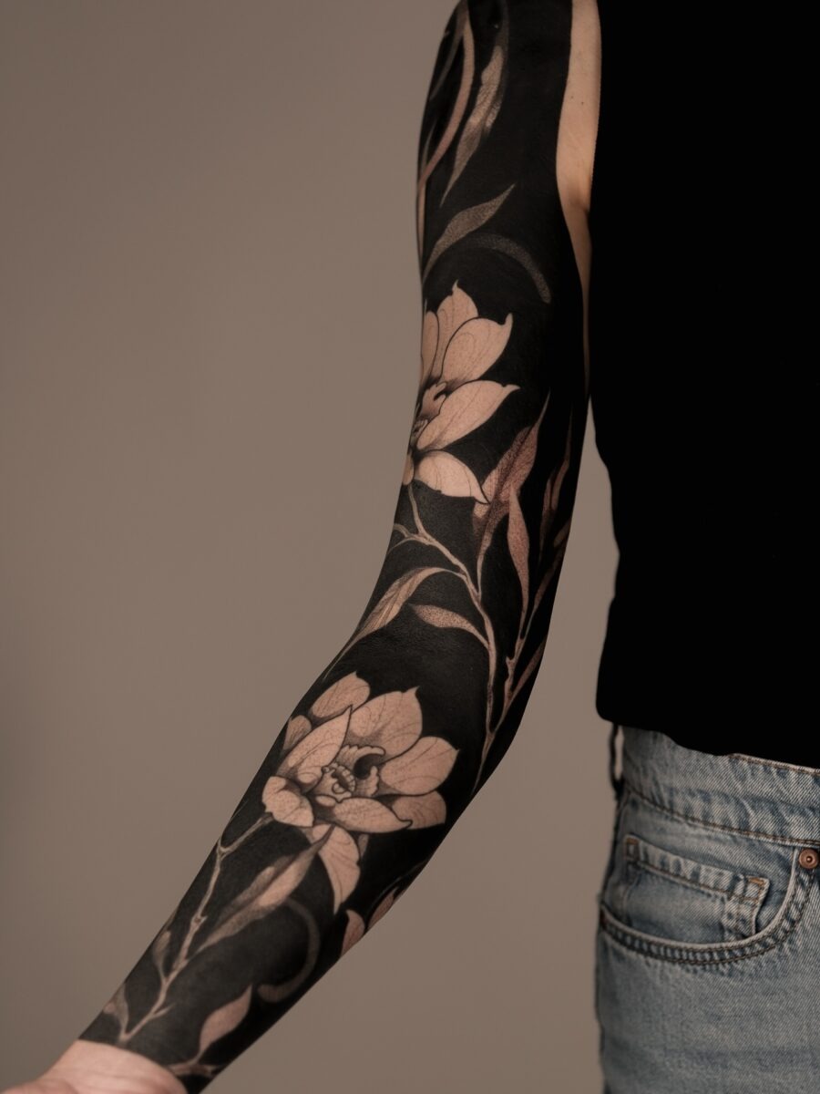 This striking black sleeve tattoo showcases intricate floral designs amidst bold shading.
