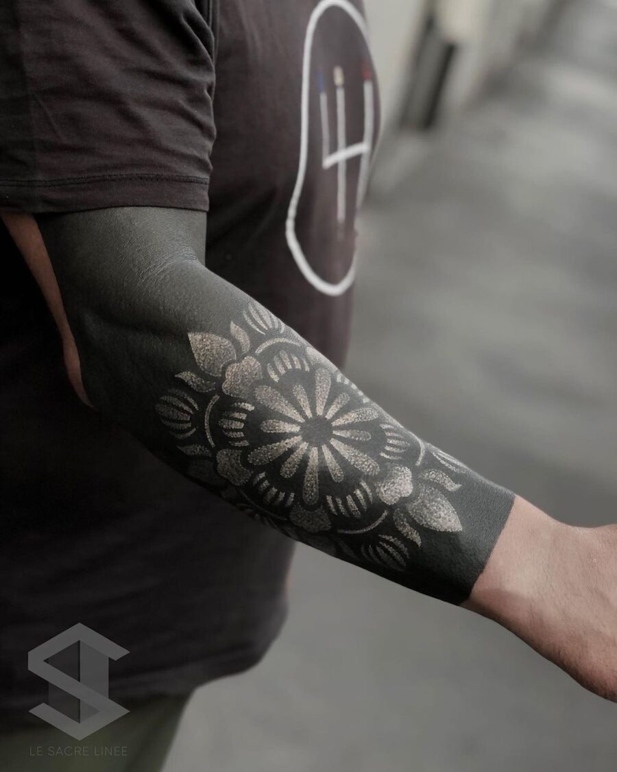 This tattoo features bold black ink intricately designed into floral patterns.