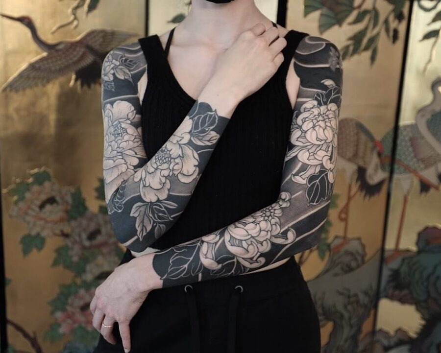 This image features a striking black sleeve tattoo adorning both arms.