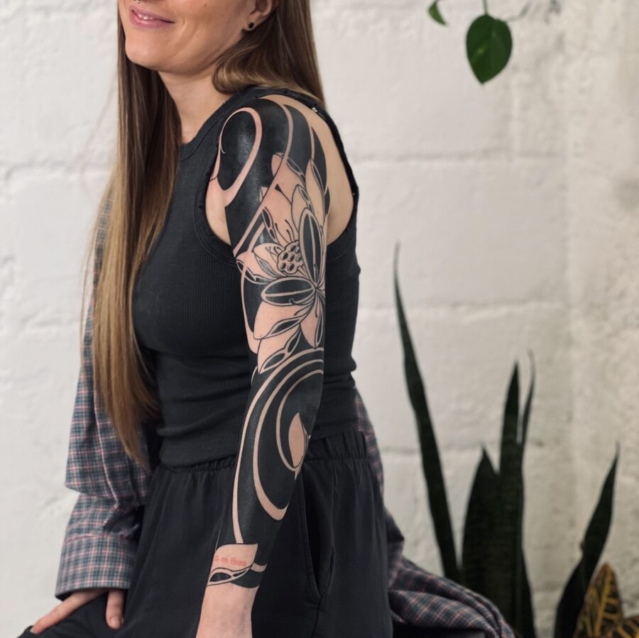This black sleeve tattoo combines intricate floral designs with bold swirls, creating a striking visual effect.