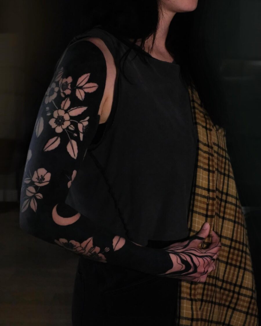 This sleeve tattoo features intricate floral patterns intertwined with negative space elements.