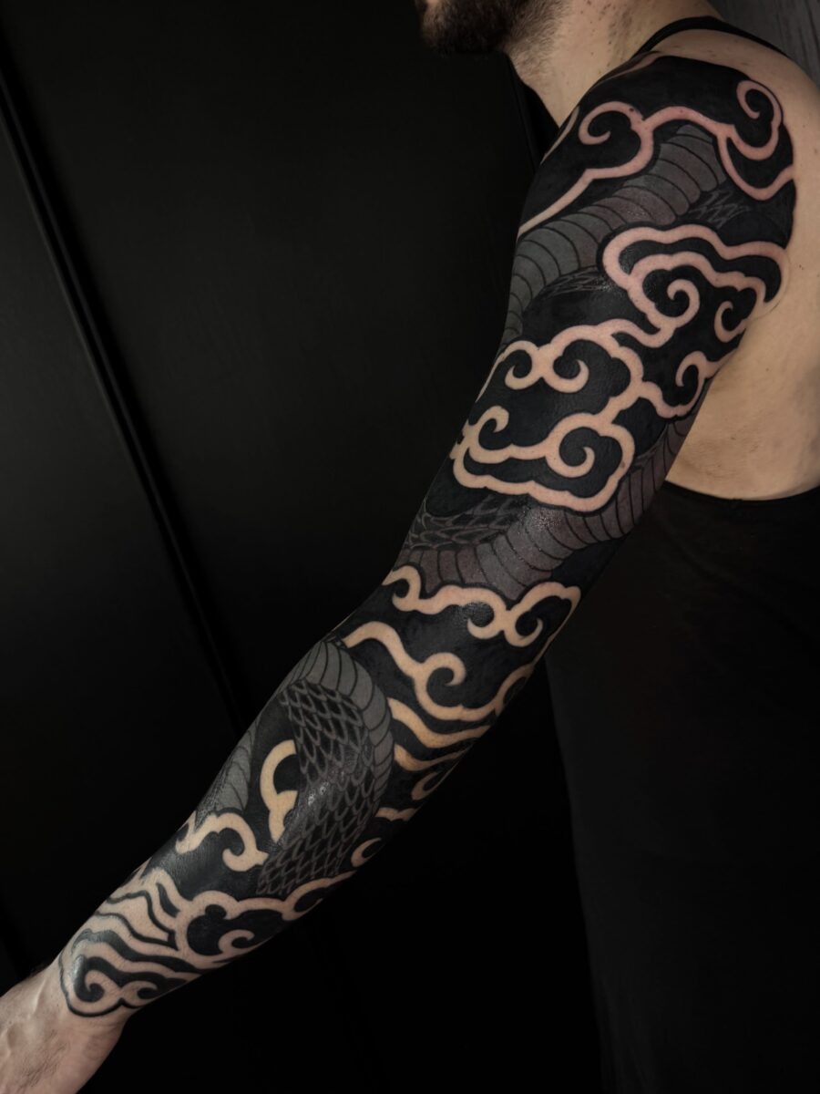 This stunning black sleeve tattoo showcases intricate wave and cloud designs, creating a dynamic visual flow.