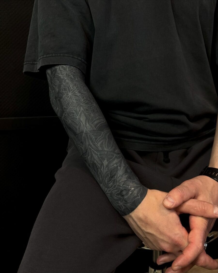 This black sleeve tattoo features a stunning, intricate design that flows seamlessly along the arm.