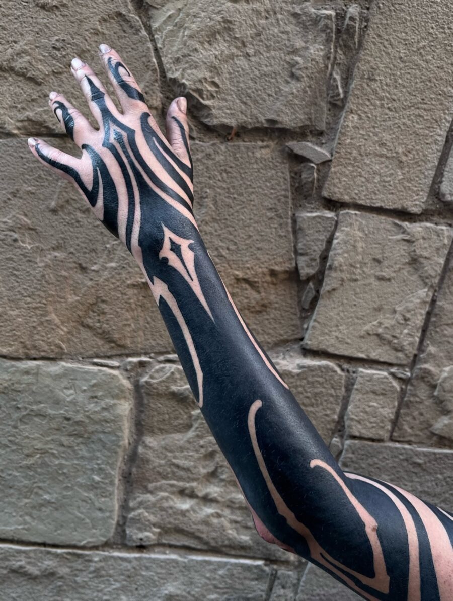 This tattoo features bold black ink wrapping around the arm, creating dynamic patterns.