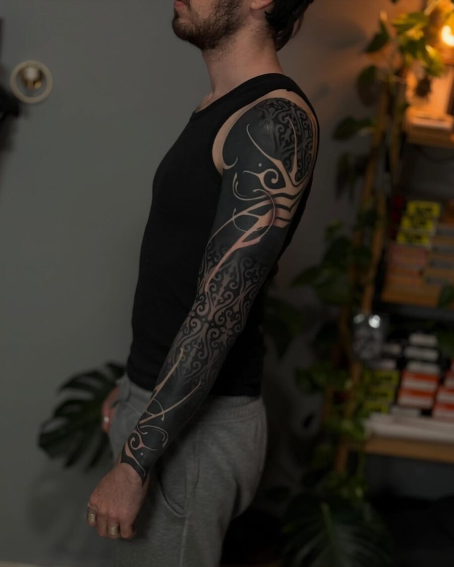 This tattoo features intricate black designs that flow elegantly along the arm.