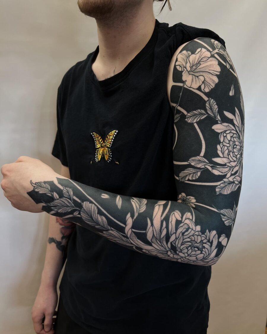 This black sleeve tattoo showcases a stunning floral design intertwined with a striking butterfly.
