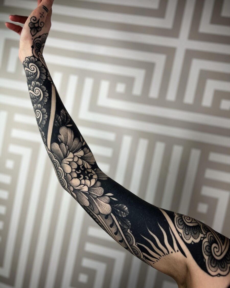 This striking black sleeve tattoo showcases a blend of floral and sun motifs, creating a smooth flow along the arm.