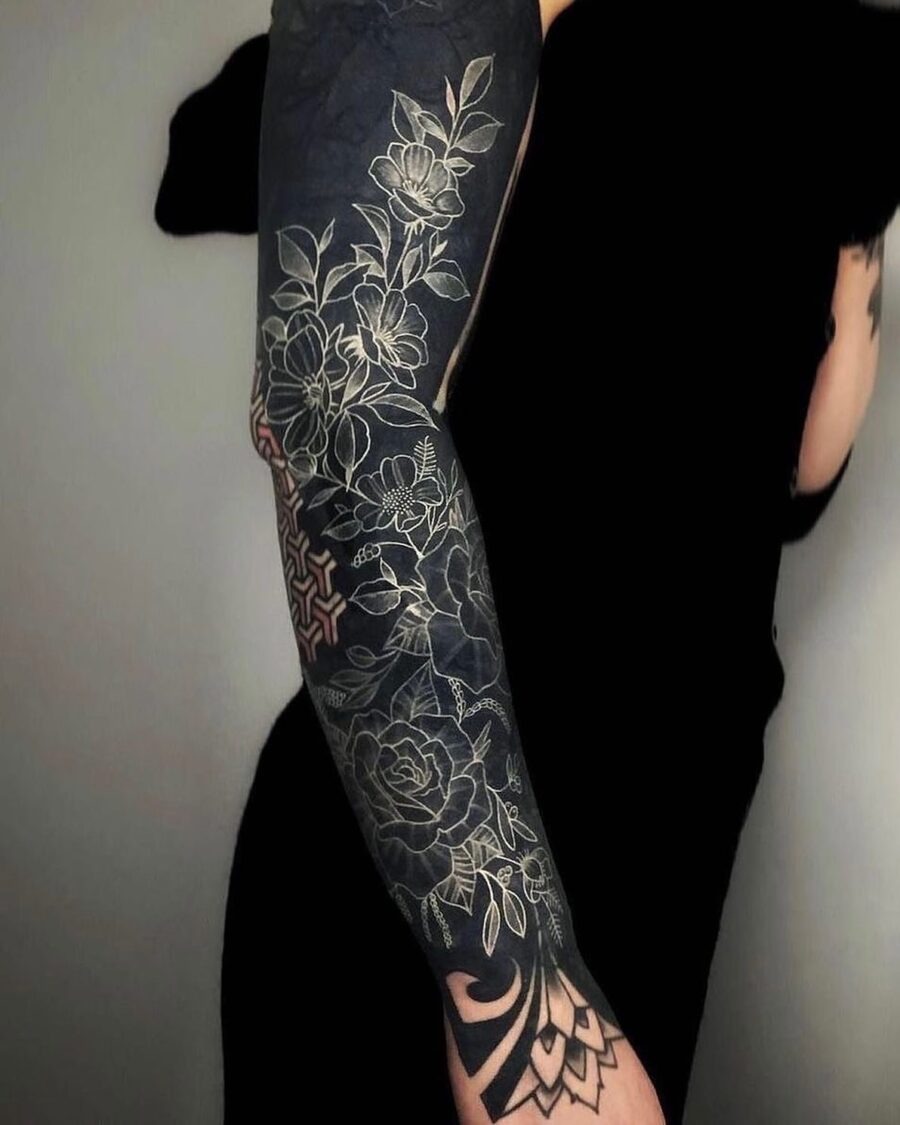 This black sleeve tattoo showcases a stunning floral design, combining detailed white ink with deep black shading.