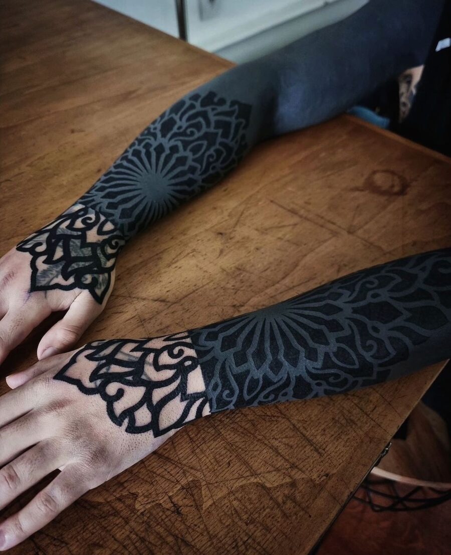 This black sleeve tattoo features intricate geometric and mandala patterns that create a bold visual statement.