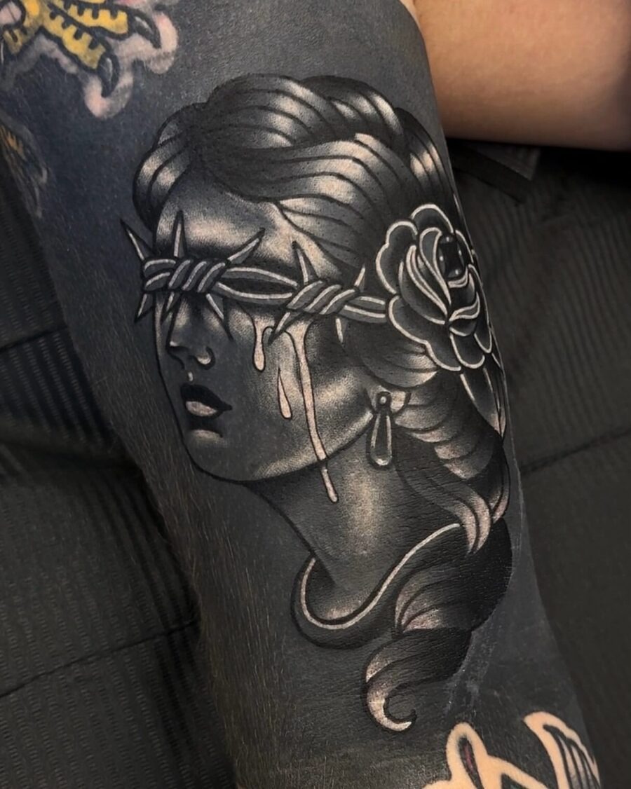 This black sleeve tattoo features a striking depiction of a woman with a blindfold, adorned with a rose.