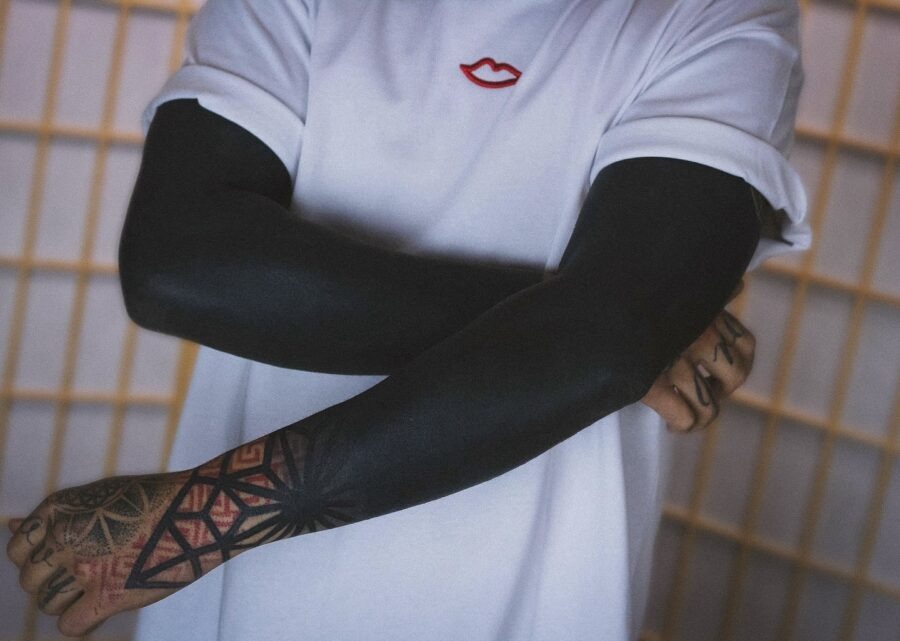 This tattoo showcases a sleek black sleeve design, harmonizing with the model's white shirt.