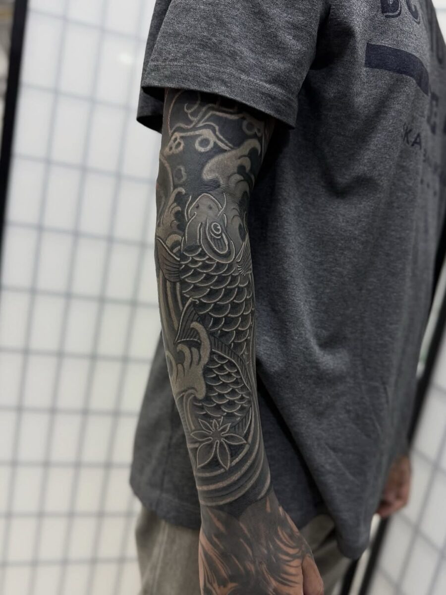 This stunning black sleeve tattoo features intricately designed koi fish, symbolizing strength and perseverance.