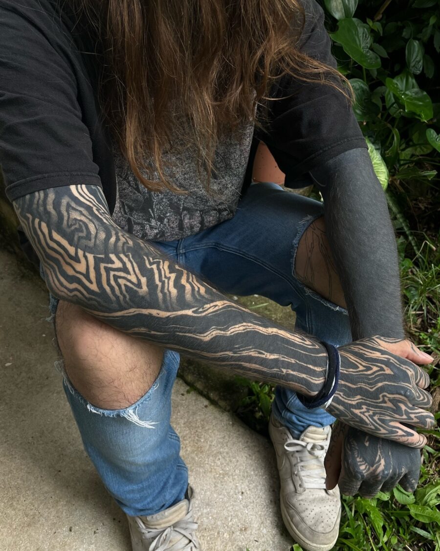This image features a person with intricate black sleeve tattoos, displaying unique designs that flow elegantly along their arms.
