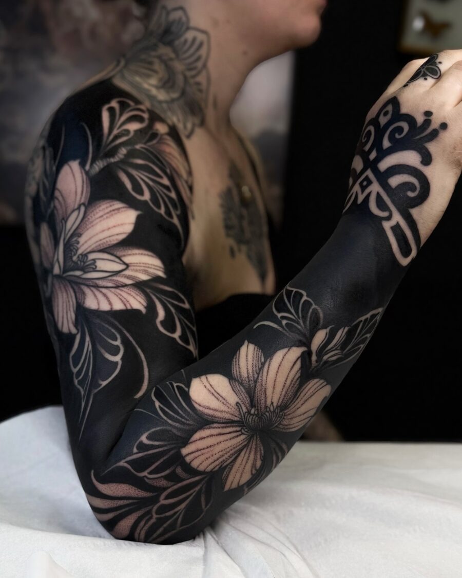 This black sleeve tattoo showcases a beautiful floral design that blends bold black ink with delicate details.