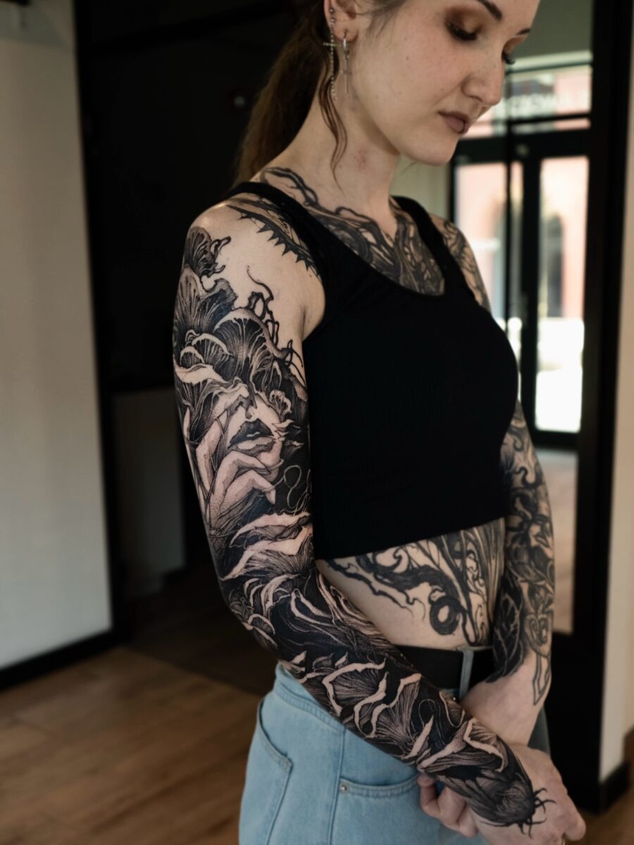 This black sleeve tattoo features a captivating mix of floral and abstract designs.