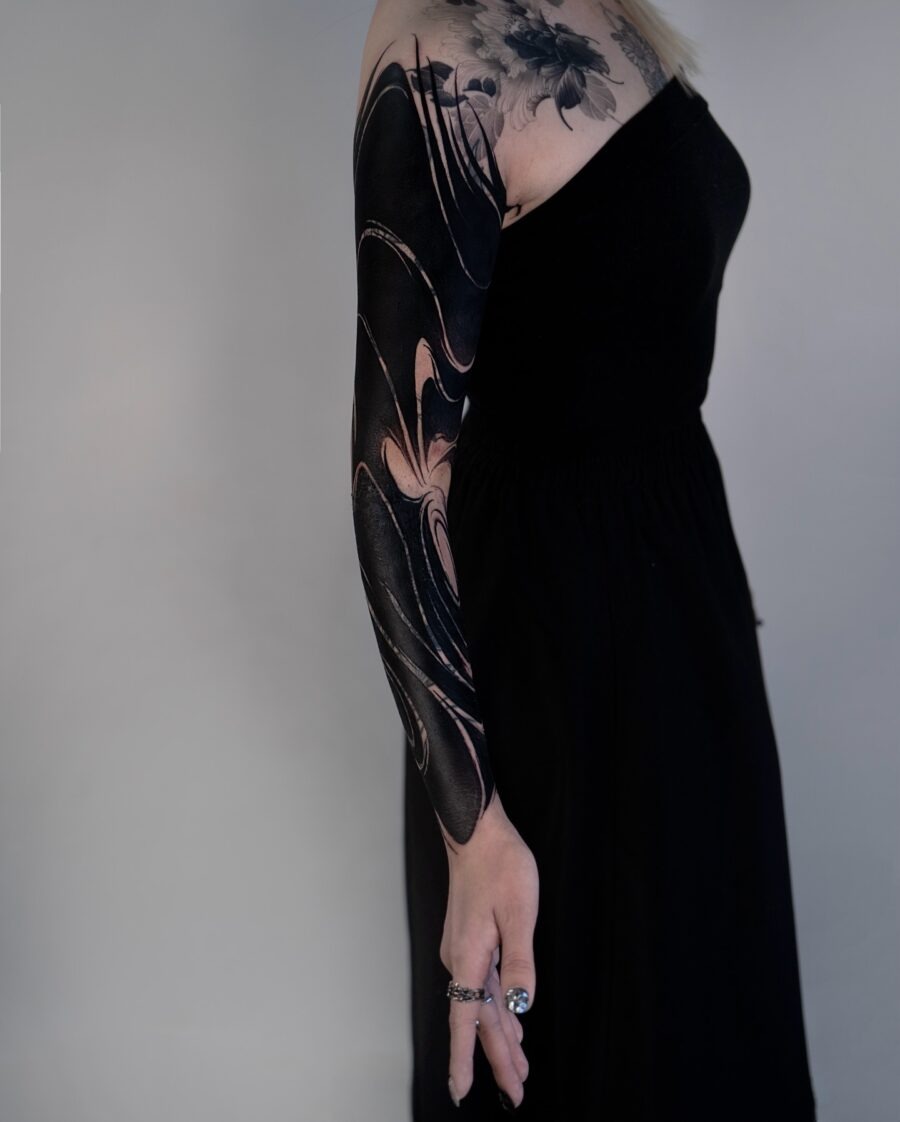 This tattoo features stunning black ink that swirls elegantly across the arm, creating a dynamic and eye-catching effect.