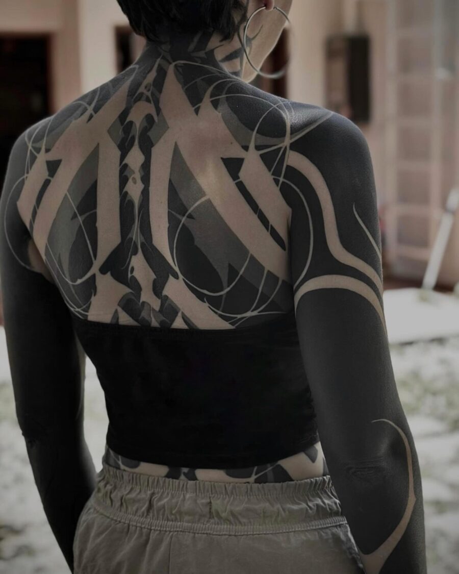 This striking black sleeve tattoo showcases a mix of geometric and abstract shapes.