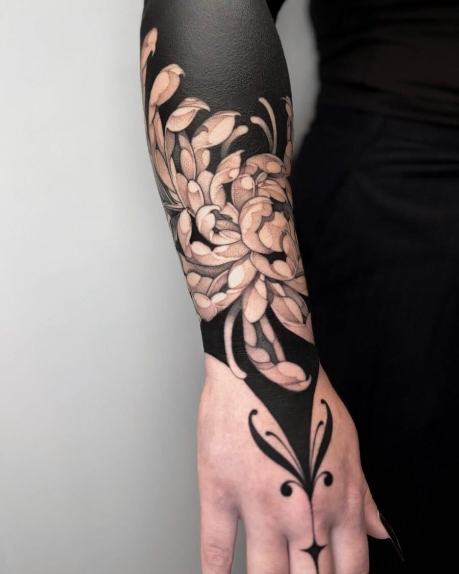 This black sleeve tattoo features intricate floral designs intertwined with negative space.