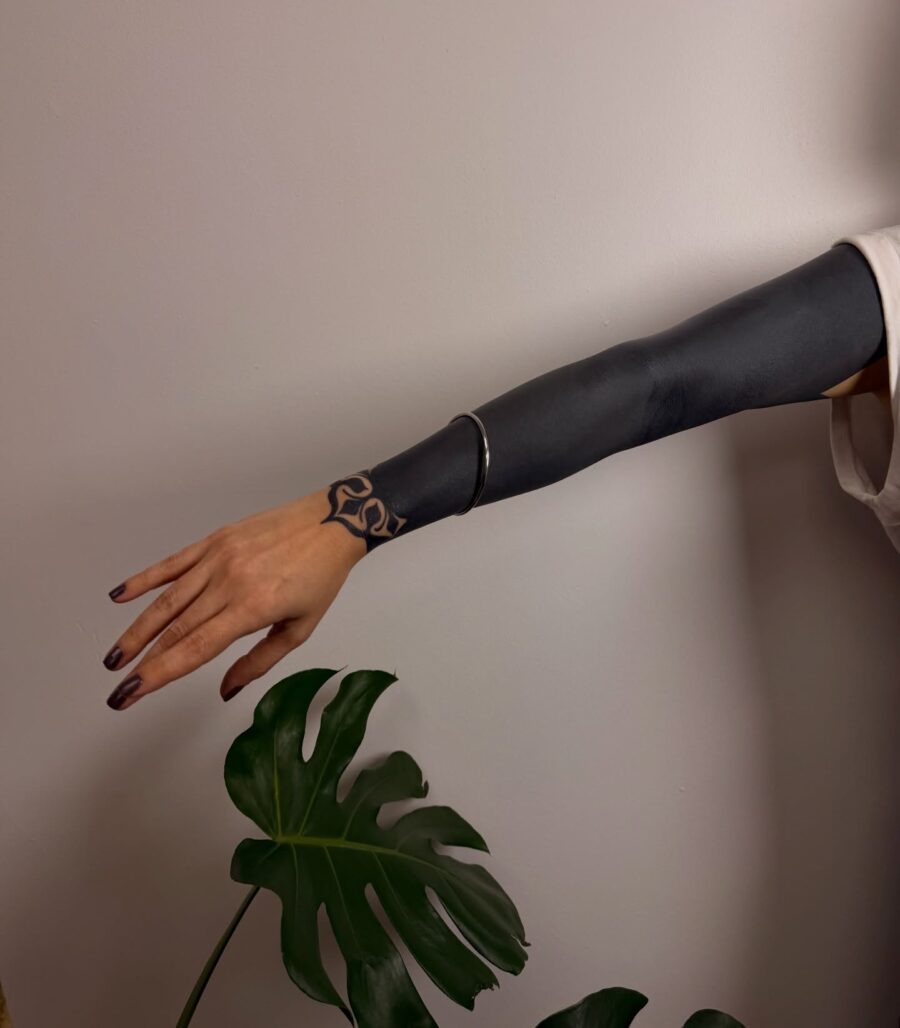 This striking black sleeve tattoo adorns an elegant arm, blending bold dark ink with delicate patterns.