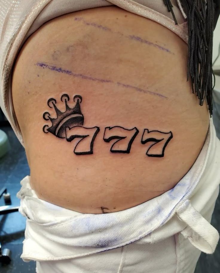 Crowned 777 Tattoo on the Hip, a tattoo design rendered in bold.
