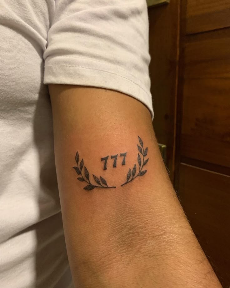 Laurel Wreath 777 Tattoo on the Arm, a tattoo design rendered in bold traditional.