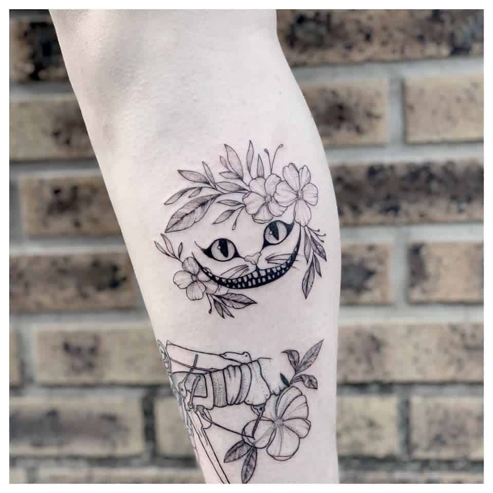 This tattoo offers a more delicate take on the Cheshire Cat, with a minimalist outline of its iconic grin and piercing eyes.