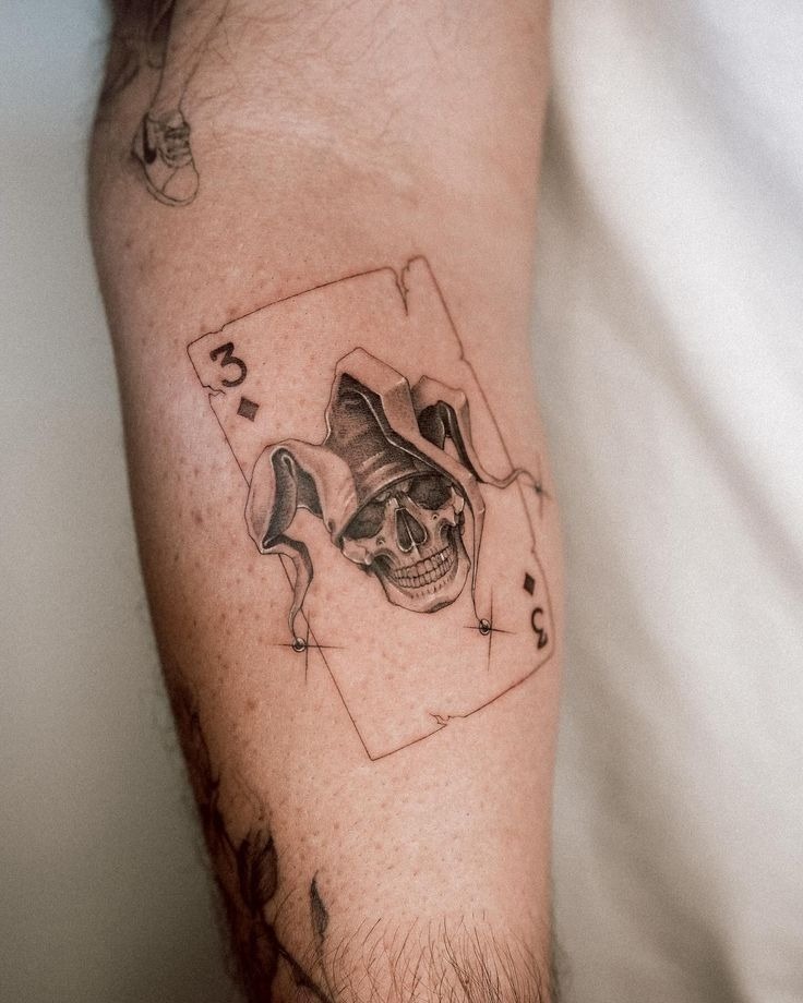Tiny Joker Card Skull, a tattoo design rendered in delicate fine-line.
