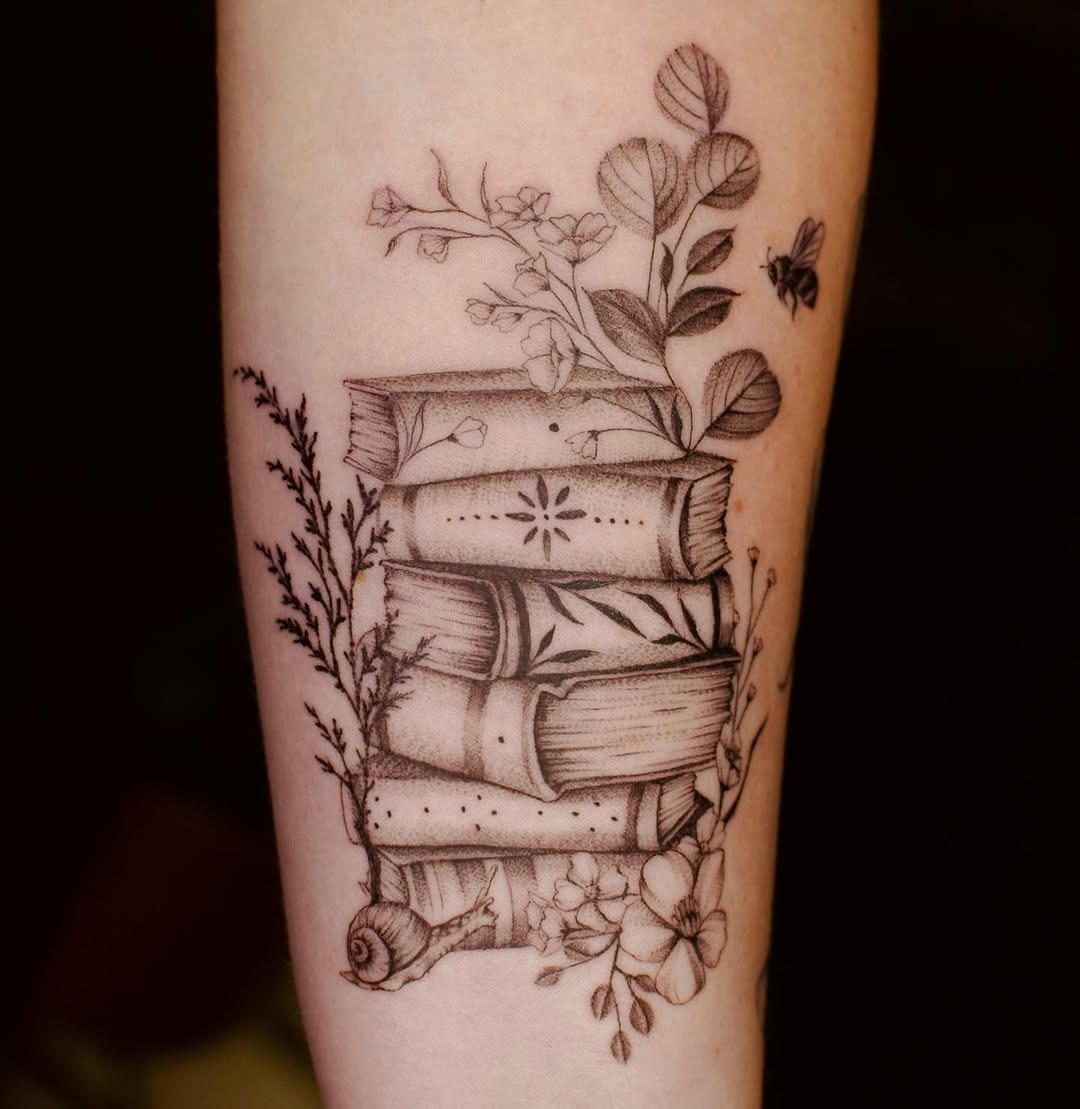 This tattoo features an intricately designed stack of books intertwined with delicate flora.