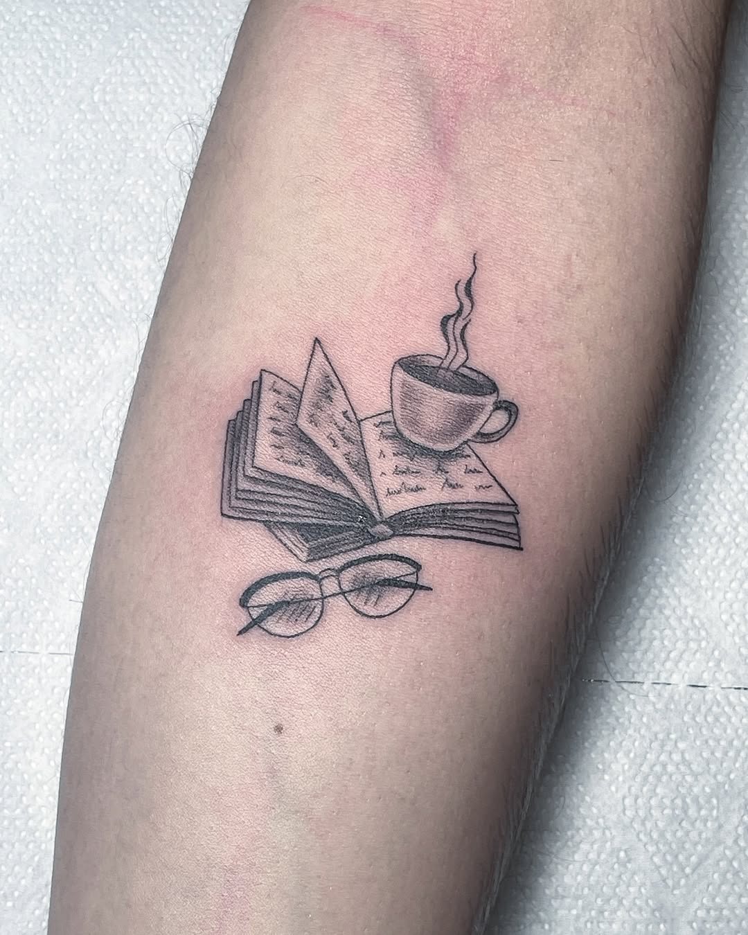 This tattoo beautifully combines an open book, a steaming cup, and glasses.