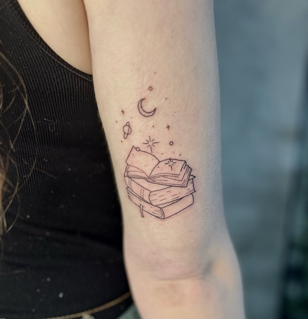 This tattoo features stacked books adorned with celestial symbols like a crescent moon and stars.