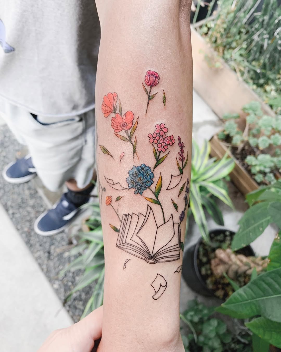 This tattoo features an open book surrounded by flowers.