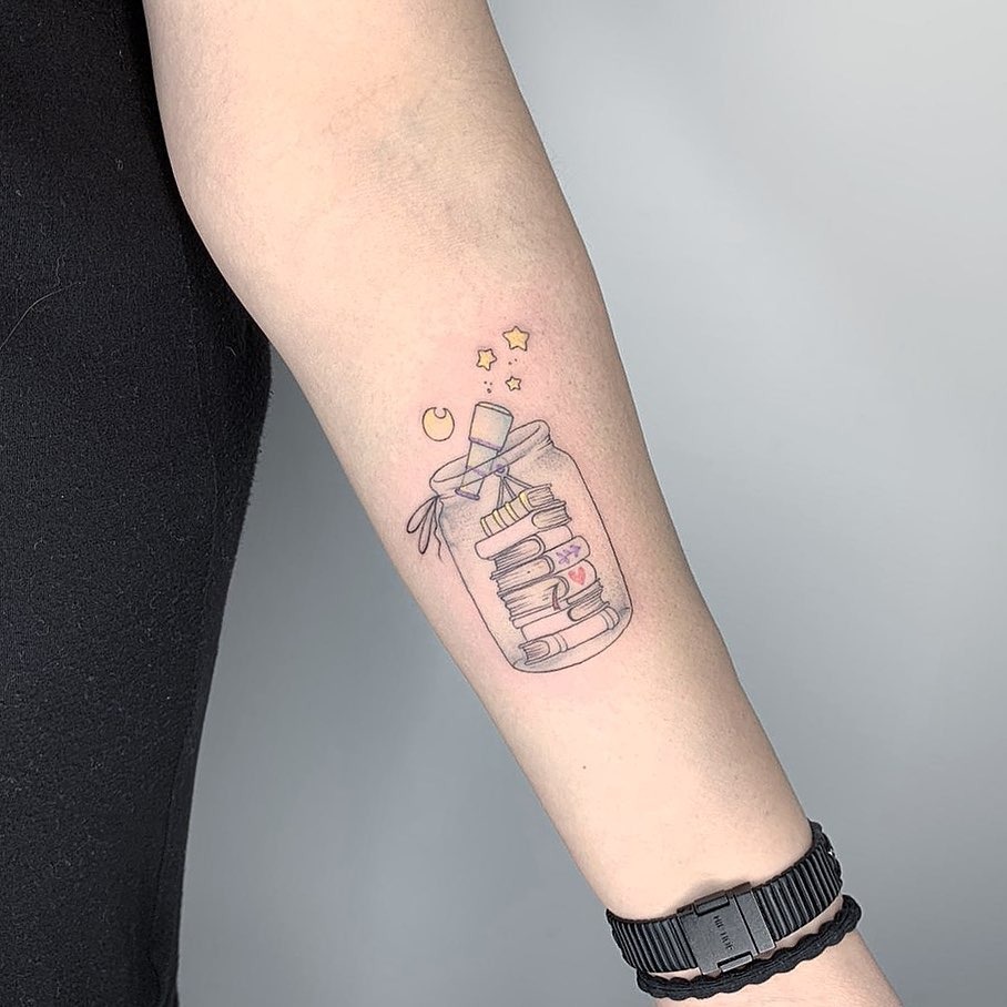 This tattoo features a charming design of stacked books inside a jar, enhanced by whimsical stars and a crescent moon.