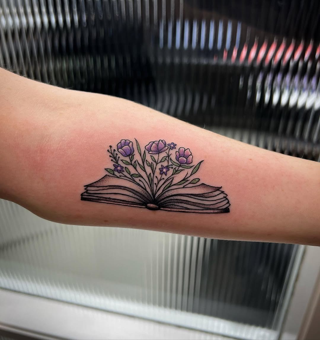 This tattoo features an open book with delicate flowers blooming from its pages.