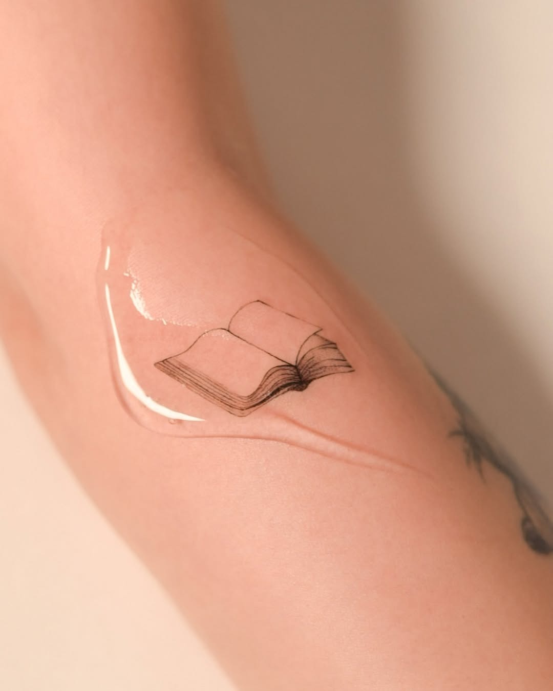 This tattoo features a simple, delicately outlined book, giving it an understated elegance.