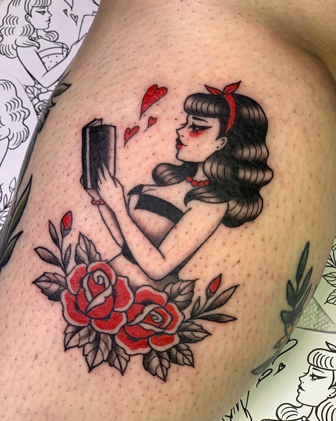 This tattoo features a stylish woman holding a book, surrounded by red roses.