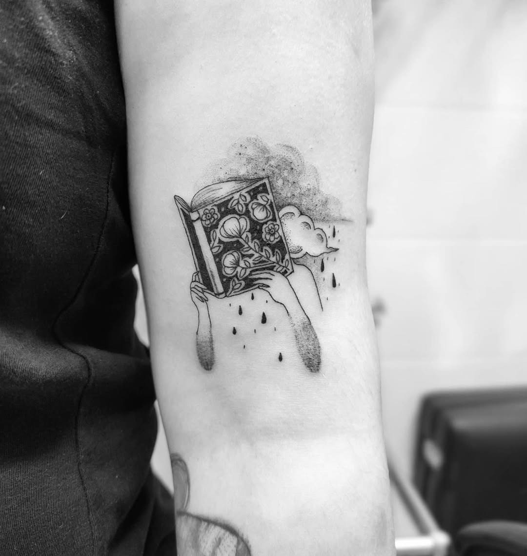 This tattoo features a person holding an ornate book with clouds above.