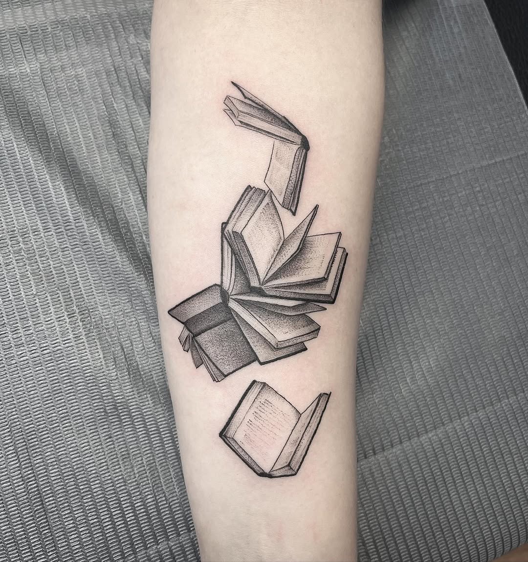 This tattoo features a beautifully rendered open book with pages in motion.