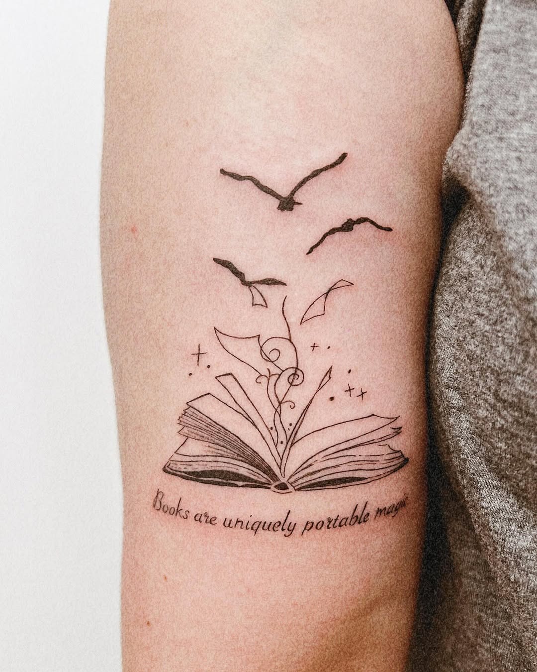 This tattoo beautifully features an open book, surrounded by swirling elements and birds in flight.