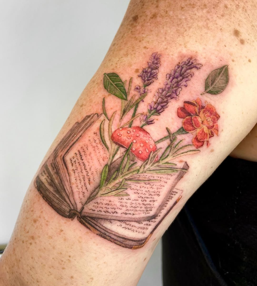 This tattoo showcases an open book bursting with flowers and a charming mushroom.