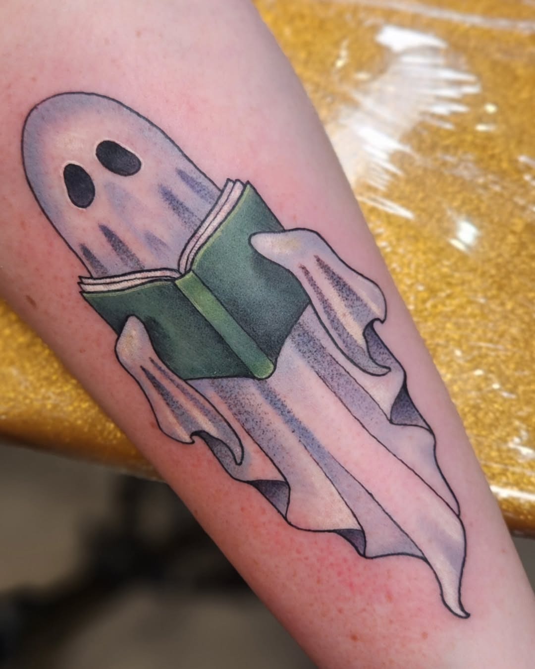 This tattoo features a playful ghost holding an open book, exuding a fun and eerie vibe.