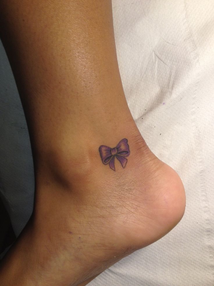 Small purple tattoo of a bow just behind the ankle Tattoo Design