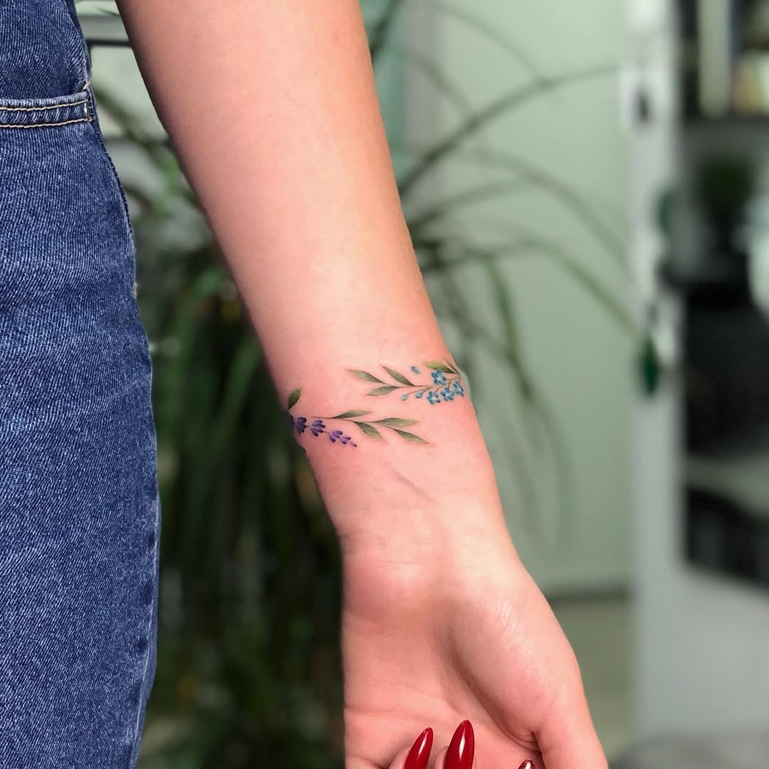 This beautiful tattoo features delicate purple and green floral elements wrapping around the wrist.